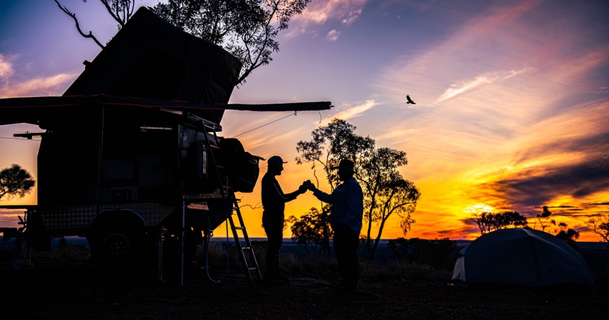 Camper trailer at sunset with people silhouetted